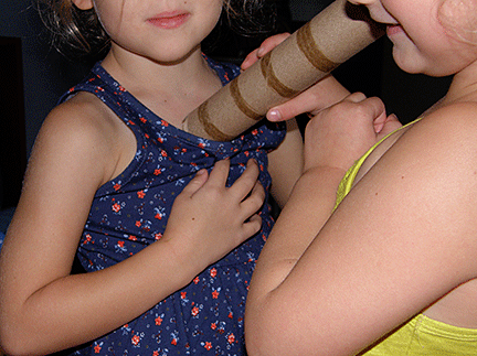 A child listens to a friend's heartbeat, using a cardboard tube.