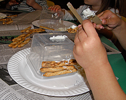 Kids build a house with breadsticks covered with icing.