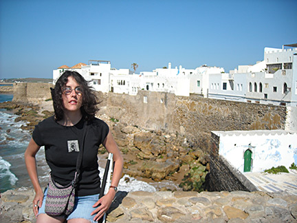 Chelsey sits on a wall with a medieval Moroccan fort in the background.