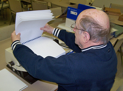 A senior volunteer binds a Braille book.