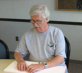 Robert Gardner sits at a table reading Braille.