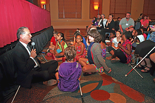 Dr. Marc Maurer sits on the floor, surrounded by children with canes.