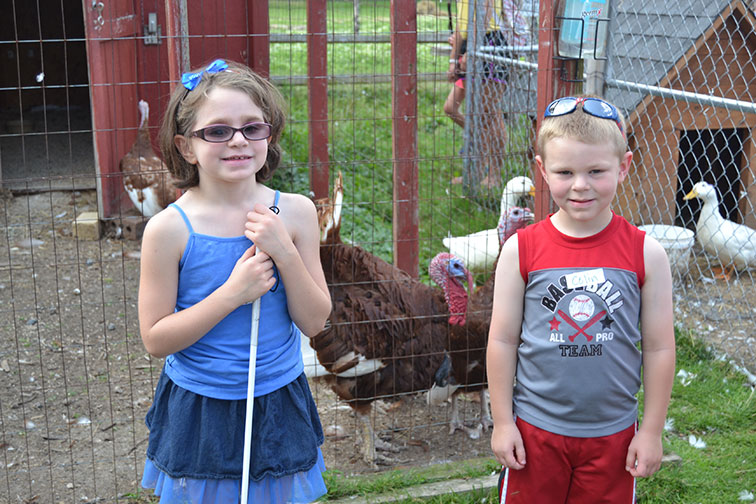 Two kids stand in a farmyard with pens of ducks and turkeys. See article entitled Youth Challenge