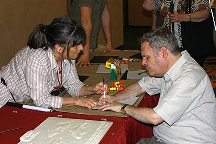 Ann Cunningham works with David Hyde of Wisconsin who is making a tactile drawing in the art room at convention.
