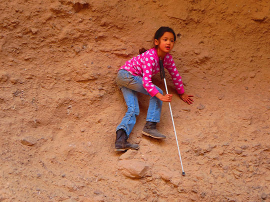 Marley Rupp climbs a rock face holding her cane.