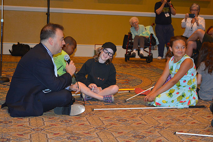 Mark Riccobono sits on the floor with children in a semicircle around him.