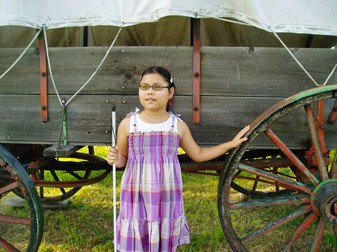 Ashleah Chamberlain stands in front of a covered wagon at a historic park.