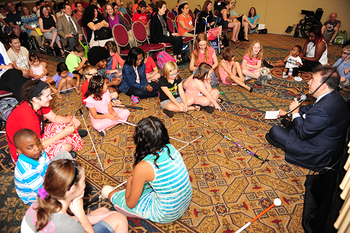 Mark Riccobono sits on the floor with a group of children at the NOPBC conference.