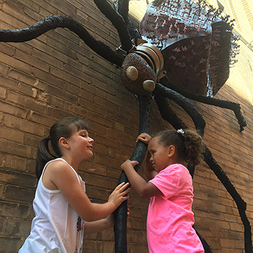Two girls examine a dangling spider sculpture.
