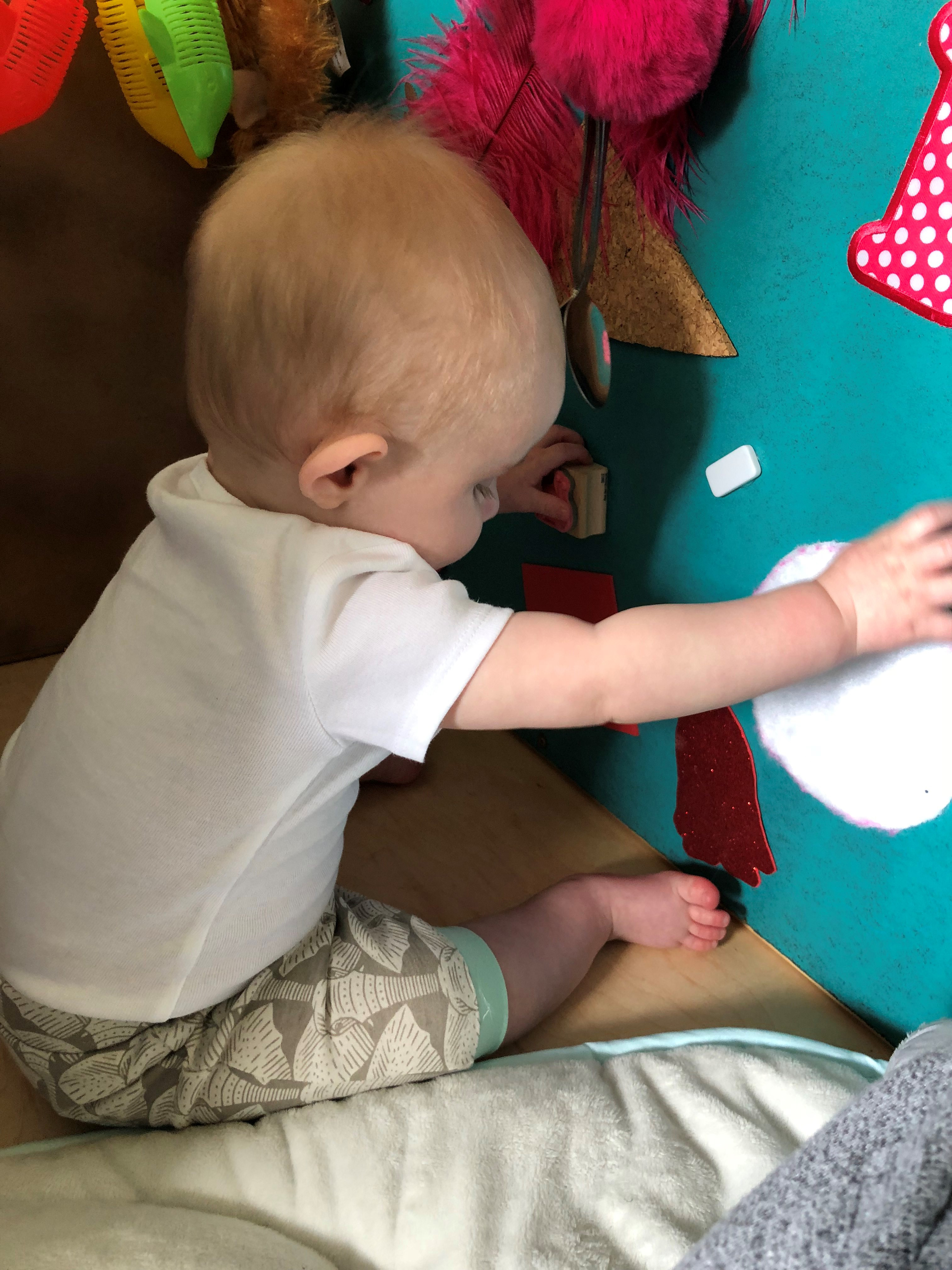 Baby Finn plays with tactile manipulatives on a board.