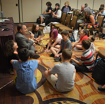 Mark Riccobono laughs with a group of children gathered around him at the NOPBC conference.]