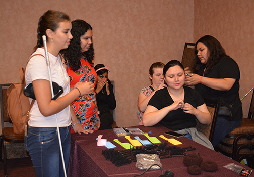 A mentor teaches a group of girls to braid hair.