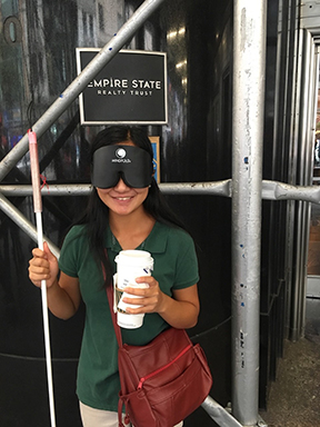 Wearing sleepshades, Ahbee Orton holds her cane in one hand and a to-go cup of hot green tea in the other.