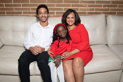 Karin Norington-Reaves sits on a couch with her son, Alex, and daughter, Rachelle.]