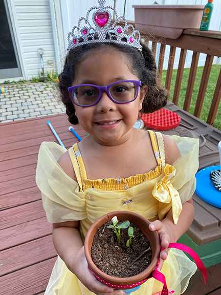 Dressed like a fairy princess, Abigail admires her sunflower plant.