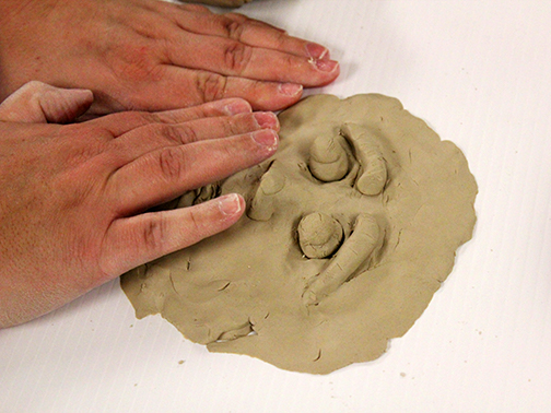 Two hands sculpt a face with clay.