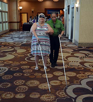 Using learning shades, Patrick Thibodeau teaches Vicki Walter-Winters to use a long white cane.