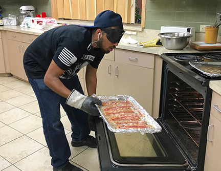 A student takes a tray of sizzling bacon out of the oven.