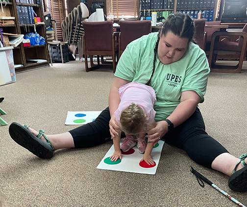 A BELL volunteer helps a small child play Braille Twister.