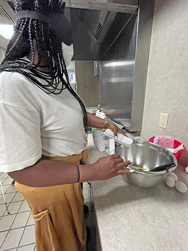 Under sleepshades a teacher measures sugar into a mixing bowl.