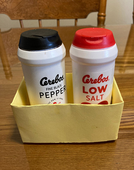 A yellow origami box containing salt and pepper shakers