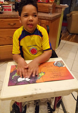 Sitting in the kitchen, Manny Perez reads a print/Braille book.