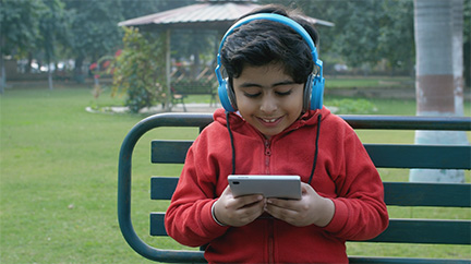 A boy sits outside, listening to a book on an audio device.