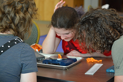 At STEM2U in 2019 Abby Duffy, Maura Loberg, and Kai Owens use a scale to weigh Cheetos.