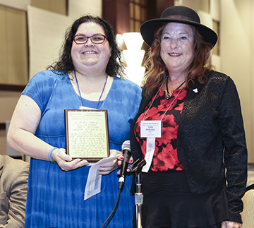 Carla McQuillan stands with Krystal Guillory who smiles and holds her Distinguished Educator of Blind Children Award. 