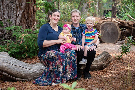 Jamie Principato Crane sits on a log with her husband and their two children.