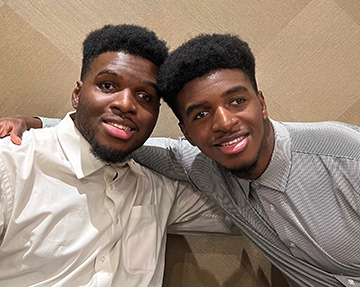 Tim and Josh Olukanni lean together affectionately.