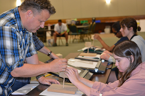 At the 2019 NFB EQ program, a participant tactually explores a wooden model as instructor Wayne Goodridge explains perspective.