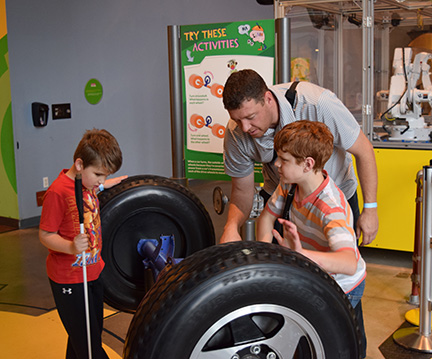 A dad shows two boys the workings of wheels and axles.