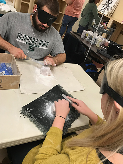 Two students under learning shades carve a stone in art class.