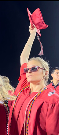 Wearing a red graduation gown, Katie Pratt holds her cap in the air.