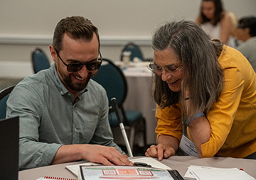 A volunteer introduces a visitor to a book with tactile pictures.
