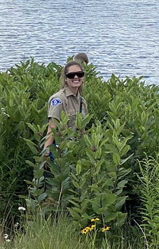 Olivia Cichowlas stands among foliage near the water&rsquo;s edge.