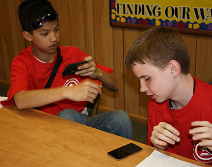 Two boys sit at a table, using their cell phones.