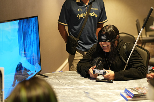 Angie Valencia of Arizona smiles as she plays an accessible video game. Check out Finding a Place in the Movement through NFB Youth Track.