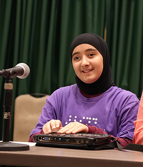 Narjis Karimipour sits with a microphone and a Braille notetaker.