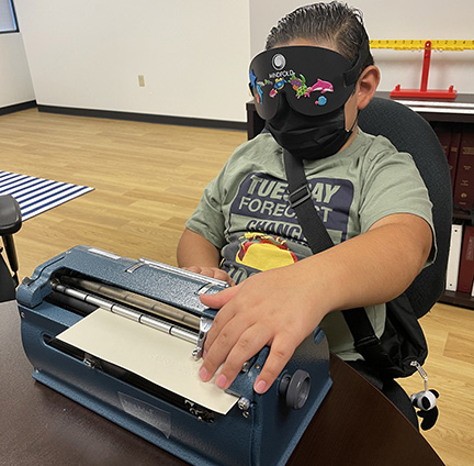 A BELL participant checks his spelling while working on a Braille writer under learning shades.