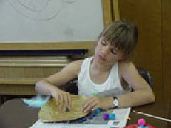 Kyra makes a metal mask at an art activity sponsored by the NOPBC at the 2002 NFB Convention.
