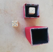 A die sits outside an empty box; the other die sits inside the lid of the box.