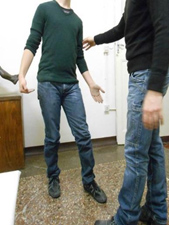 Two people standing, facing each other. On the left, the guided person mimics Riace Bronze's pose.