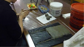 A preparation of the clay surface. Then, the reproduction of the plaster bas-relief is made, depicting the Kouros from Melos and Statue B of the Riace Bronze.