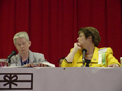 Sharon Maneki reads a resolution in Braile at the mictophone while Sharon Omvig listens