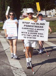 NFB of Florida Polk Chapter members Donna Kelly, Joe Dobbs, and April Stanlry cross a busy intersection durinh the chapter's White Cane Walk.