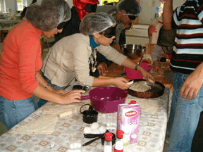 Students work on developing cooking skills at a large table. The woman in the middle is fitting pastry into a pan.