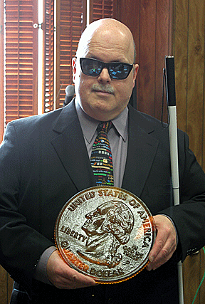 Robert Jaquiss examines an enlarged resin Braille coin created with an Objet 3D printer.