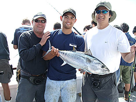 After a successful fishing trip, Gordon Chan stands victorious on the right, while his friend Alex triumphantly displays the day�s catch in the center, with Captain Mike on the left.